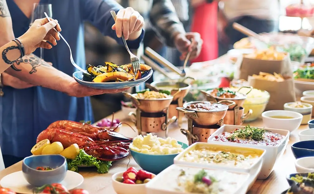 Personas haciendo cola y sirviéndose comida de un bufé en sus platos.