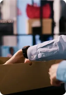 A close-up of a person placing items into a cardboard box, preparing products for packaging or shipment in a retail or e-commerce setting.