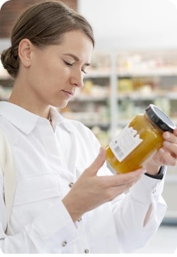 A consumer is examining a jar of food in a grocery store, carefully reading the product label for nutritional or ingredient information.