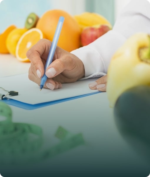 A student writing notes on a clipboard with fresh fruit, representing nutrition and dietetics programs.