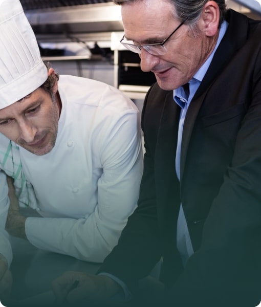 A Food Consultant in a suit reviewing documentation with a chef in a professional kitchen.