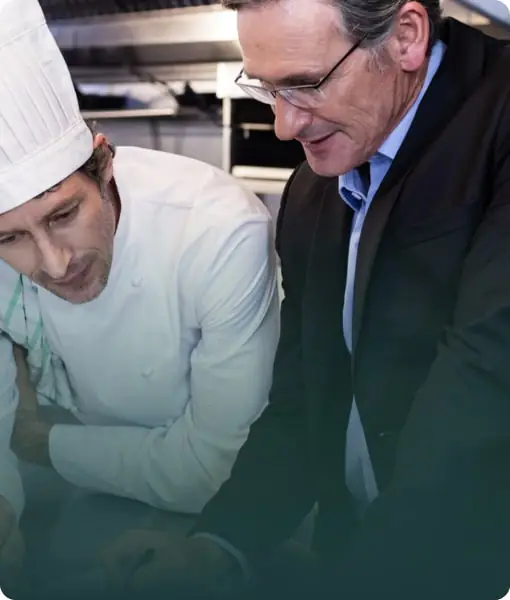 A Food Consultant in a suit reviewing documentation with a chef in a professional kitchen.